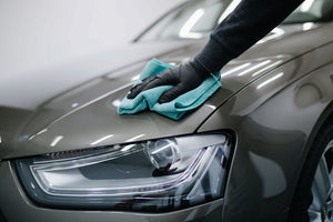 Eine Person mit Handschuhen reinigt die Motorhaube eines Autos mit einem Mikrofasertuch