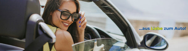 Eine Frau mit Sonnenbrille sitzt lächelnd in einem Auto.