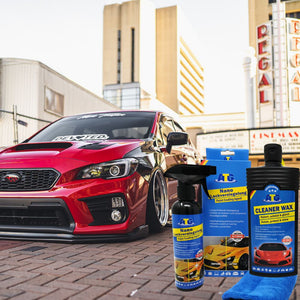 Ein rotes Auto, das auf einer Backsteinstraße in der Nähe von Gebäuden geparkt ist, präsentiert Produkte der ATG GmbH & Co. KG, wobei das ATG® Auto-Sparset Lack - Pflege DUO prominent im Vordergrund abgebildet ist.
